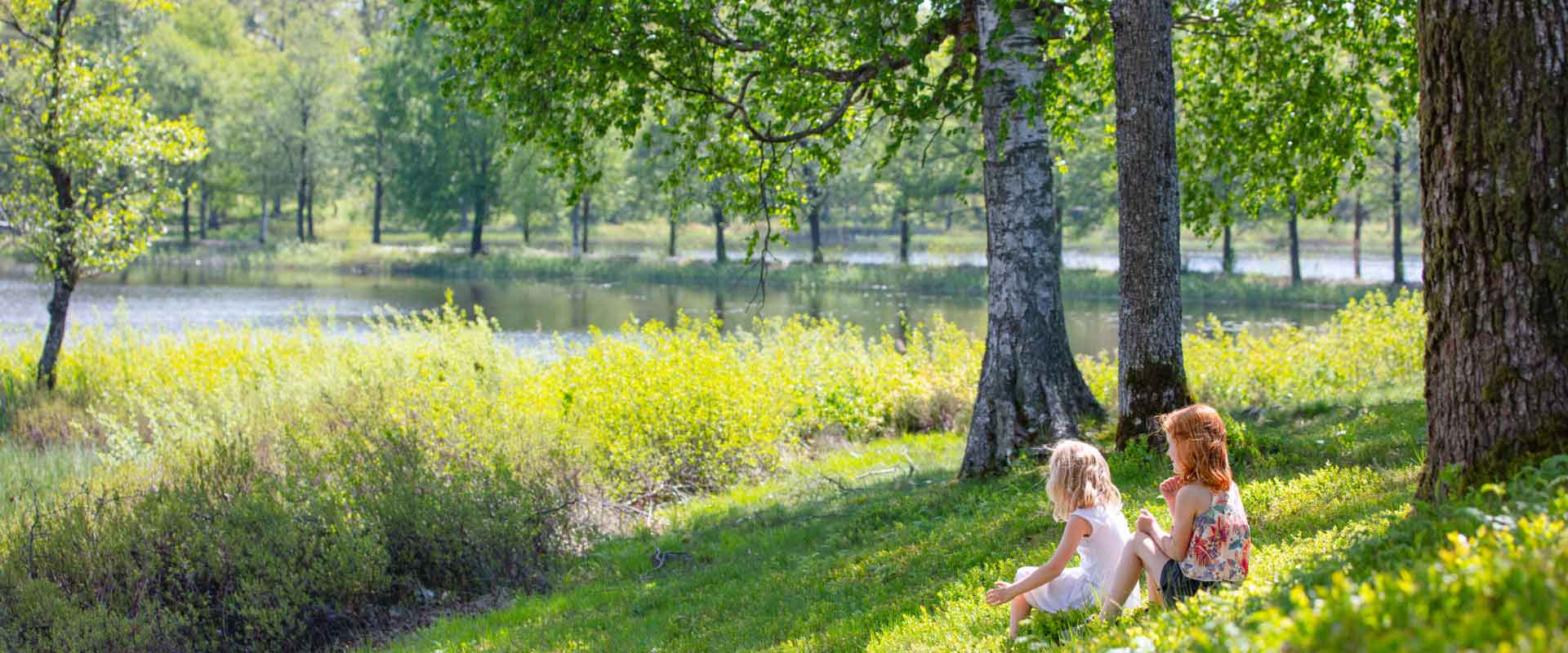 Kinder sitzen im Gras am See in Schweden